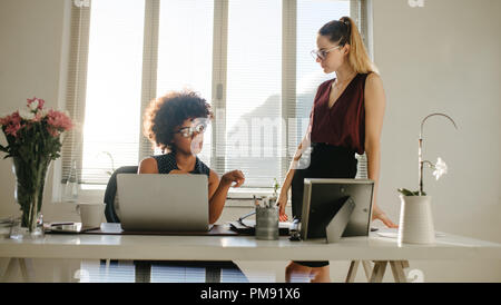 Portrait of two businesswomen discussing work in office. Les jeunes femmes parler de nouveau projet dans un bureau moderne. Banque D'Images