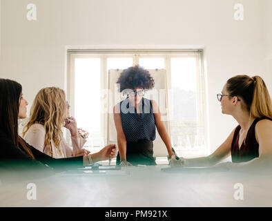 Jeune femme d'Afrique partage ses idées aux collègues femmes assis autour d'une table de conférence dans un bureau moderne. Groupe de femmes ayant une réunion i Banque D'Images