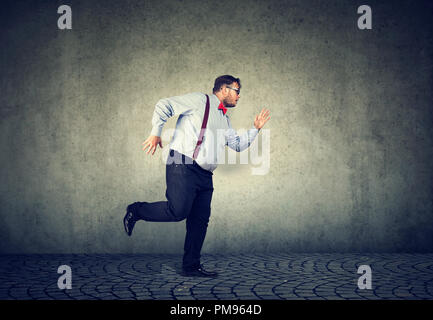 Vue latérale du businessman in chubby tenue formelle d'exécution de l'avant d'être en retard sur fond gris Banque D'Images