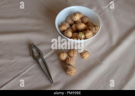 Casse-noisette et les noix dans un bol sur une table couverte d'une nappe. En-cas sur la table de cuisine. Fond clair. Banque D'Images