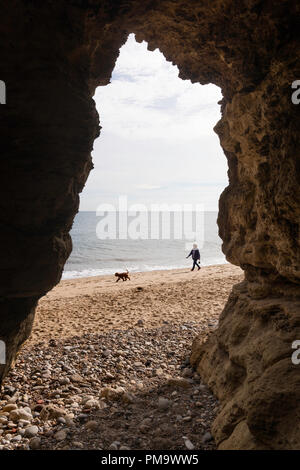 Woman walking dog le long de la plage encadrée par une grotte, Seaham, Co Durham, England, UK Banque D'Images