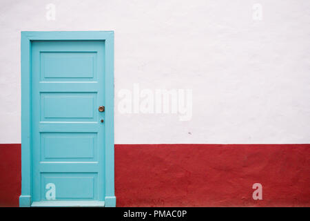 Une porte bleu turquoise (boiseries) dans un mur blanc avec une bordure rouge. La porte est à gauche avec l'espace vide sur la droite du châssis Banque D'Images