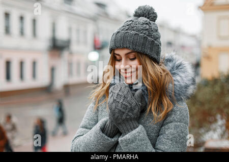 Pretty woman smiling in a hat tricoté des mitaines et un sur un arrière-plan de la ville. Banque D'Images