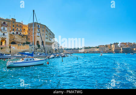 La vue de Vittoriosa marina sur le vieux bâtiments en pierre de Senglea (L-Isla), bateaux et yachts à sa rive et l'énorme remparts de La Valette sur le Banque D'Images