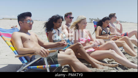 Groupe de six hommes femmes amis assis sur la plage en maillot de bain et bikinis Banque D'Images