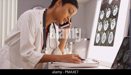 Femme médecin noir sur le téléphone et de lecture x-ray scans Banque D'Images