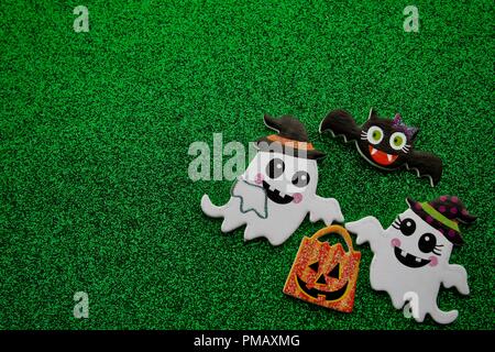 Deux fantômes transportant une citrouille trick or treat sac avec une chauve-souris volant au-dessus des noirs sur fond vert. Banque D'Images