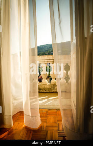 Rideaux filet qui soufflent dans le vent comme ils donnent sur la vieille Europe hôtel balcon avec vue sur la création d'une ambiance romantique à Opatija, Croatie Banque D'Images