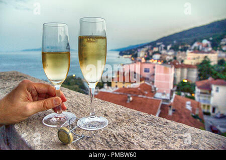 Deux verres remplis avec la main d'un homme tenant un verre sur un balcon donnant sur l'hôtel resort village et la mer Adriatique en Croatie Banque D'Images