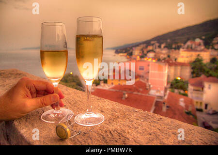 Deux verres remplis avec la main d'un homme tenant un verre sur un balcon donnant sur l'hôtel resort village et la mer Adriatique en Croatie Banque D'Images