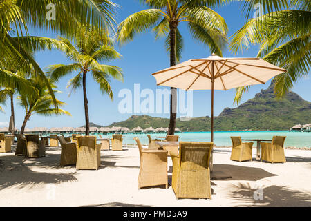 Chaises et une table sous un parasol en chaume sur une plage de sable avec vue sur le lagon tropical Banque D'Images