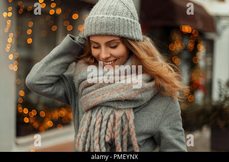 Belle fille heureuse à la mode dans le style vintage avec manteau à la mode en tricot chapeau avec écharpe près de feux jaunes dans la rue Banque D'Images