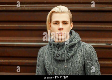 Blonde à la mode homme avec une coiffure dans un tricot pull élégant se trouve à proximité d'une paroi métallique Banque D'Images