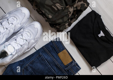 Mode élégante collection de vêtements d'été pour hommes sur un fond blanc. Baskets blanches avec un jean bleu, une chemise militaire et un T-shirt noir sur un wo Banque D'Images