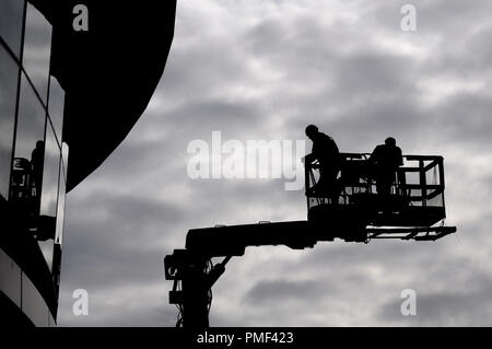 Deux travailleurs de la construction en silhouette contre le ciel gris sur une rampe de levage hydraulique Banque D'Images