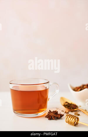Le thé noir dans une tasse en verre avec cuillère d'or avec des herbes, du balancier et l'anis sur en dessus de table. Fond rose féminin avec copie espace. La profondeur de l'Étroit Banque D'Images