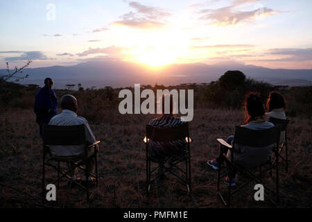 Un guerrier Massaï se tient debout avec sa lance tandis que les touristes s’assoient avec leur guide local et profitent du coucher de soleil sur la zone de conservation de Ngorongoro en Tanzanie, Afrique orientale Banque D'Images