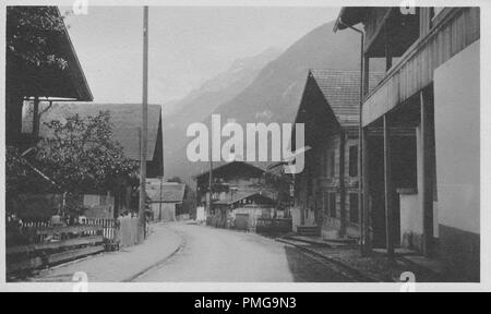 Photographie en noir et blanc sur papier cartonné, avec une image d'un milieu rural, rue Européenne à plusieurs étages, avec des chalets en bois, et avec des montagnes, peut-être les Alpes, se profilant dans l'arrière-plan, probablement perçus comme un souvenir touristique lors d'un voyage en Europe du Nord (probablement une région du Rhin Supérieur, près des frontières de l'Allemagne, la Suisse et la France), 1910. () Banque D'Images