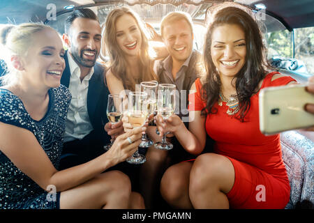 Party People dans une limousine avec des boissons en tenant un téléphone avec selfies Banque D'Images