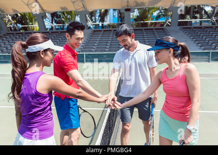 Quatre jeunes joueurs de tennis, mettant les mains ensemble avant un match mixte en double Banque D'Images