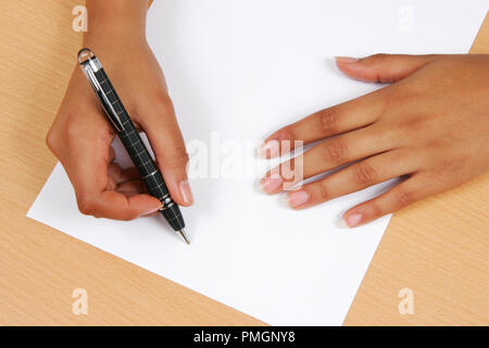 Womans mains sur un bureau en bois reposant sur un morceau de papier et d'un tenant un stylo Mont Blanc prêt à écrire Banque D'Images