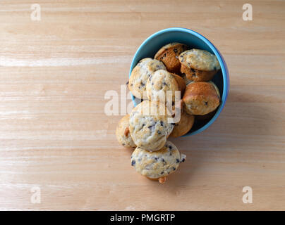 Plusieurs des petits muffins aux bleuets un bol bleu sur le côté sur une table en bois. Banque D'Images