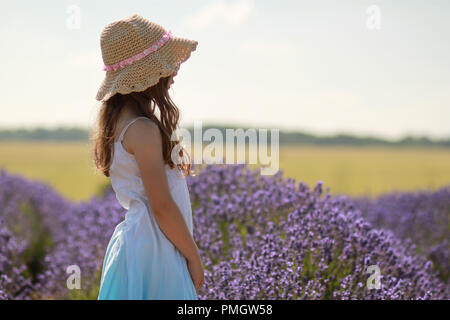 Petite fille, je suis debout sur le côté dans un champ de lavande portant un chapeau. Banque D'Images