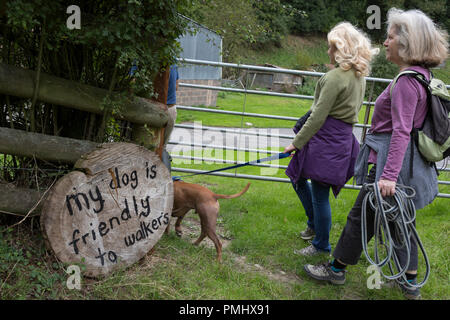 Les marcheurs du pays passent par une porte avec leur chien, à côté d'un signe rassurant ceux qui entrent dans un champ qu'un animal est à proximité de Walker, le 10 septembre 2018, près de Lingen, Herefordshire, Angleterre, Royaume-Uni. Banque D'Images