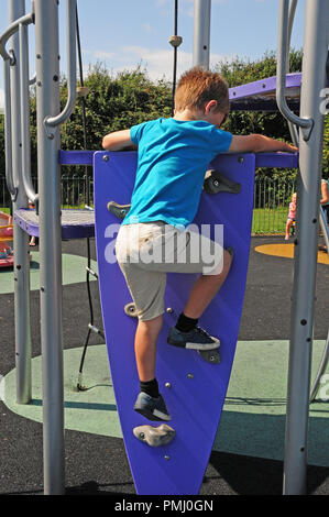 Garçon de sept ans l'escalade un mur d'escalade jusqu'à une diapositive dans un parc de jeu. Banque D'Images