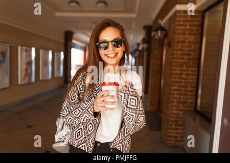 Heureux mode femme avec du café dans l'élégant quartier de lunettes de soleil et une veste à la mode des sourires et des promenades dans la ville Banque D'Images