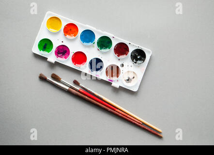 Mise à plat de la palette d'aquarelle et pinceaux sur fond gris. Vue d'en haut. Banque D'Images