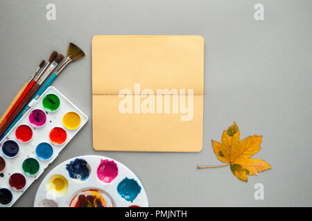 Mise à plat de la palette d'aquarelle, pinceaux, sketchbook et les feuilles d'automne. Bonjour automne concept. Banque D'Images