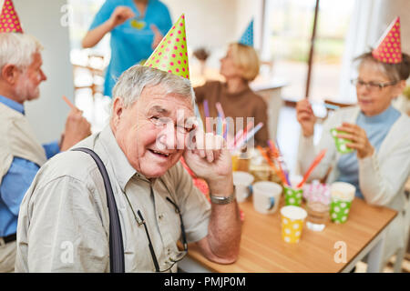 Vieil homme avec chapeau de fête célèbre l'anniversaire avec des amis en maison de soins infirmiers Banque D'Images