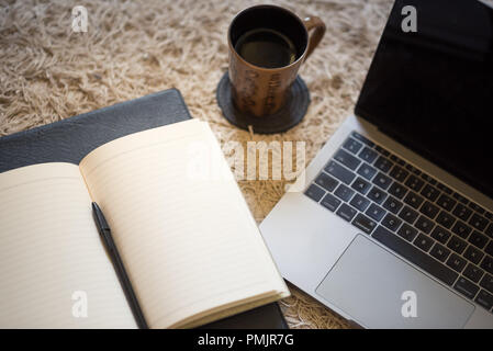 Une vue du haut vers le bas d'un journal, avec une lumière chaude qui tombe sur les pages blanches, à côté d'une tasse de café et un ordinateur portable Banque D'Images