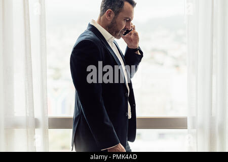 Vue latérale du businessman talking on cell phone. L'homme dans chambre d'hôtel après avoir discuter par téléphone. Banque D'Images