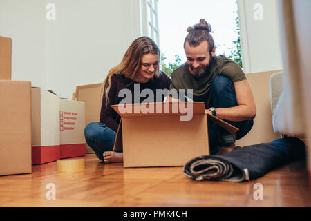 Couple heureux d'ouvrir leurs articles après avoir déménagé dans une nouvelle maison. Smiling man and woman looking at leurs articles emballés dans une boîte. Banque D'Images