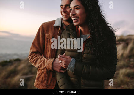 couple de voyage en hiver porter debout dehors ensemble sur la falaise et regardant la vue. Homme et femme regardant la vue du sommet de la montagne et riant Banque D'Images