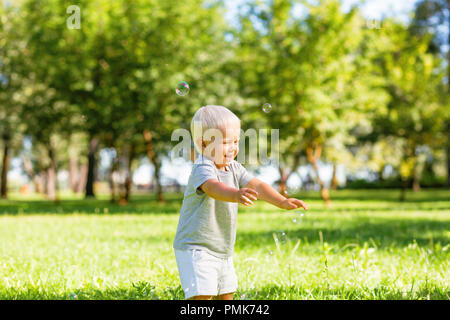 Heureux l'enfant attraper des bulles de savon dans le jardin Banque D'Images