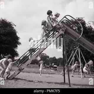 Années 1950, historiques, les jeunes chiidren en extérieur dans un aire de jeux en hauteur sur les étapes d'une diapositive métal traditionnel, England, UK. Banque D'Images