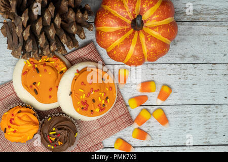 Le sucre glacé Orange et à l'automne thème de l'Halloween cupcakes - maïs bonbons dispersés. Cônes de pin et de citrouilles, fond de bois. Concept pour l'automne Banque D'Images