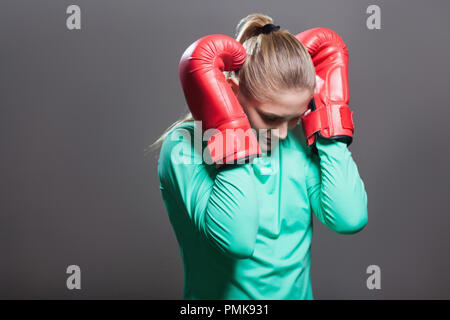 Triste jeune athlète femme aux cheveux recueillis en position debout, tenant la tête en bas et part en boxe gants rouge près des oreilles après coup. Piscine Banque D'Images