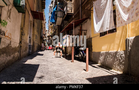 Homme assis à l'extérieur chambre dans une vieille rue étroite dans le centre de la ville, Naples, Italy, Europe Banque D'Images