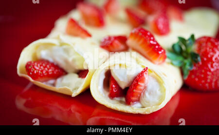 Crêpes aux fraises avec de la crème fouettée sur une plaque rouge Banque D'Images