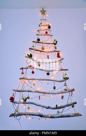 Tenture murale moderne créative faites de bois flotté d'arbre de Noël avec des lumières et des décorations suspendues et babioles Banque D'Images