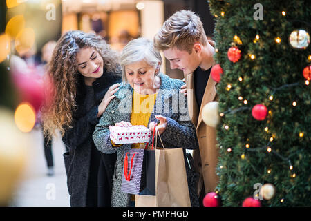 Un jeune couple giving a present à grand-mère dans un centre commercial au moment de Noël. Banque D'Images