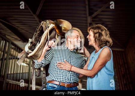 Un couple d'une selle de cheval sur ses épaules dans une étable. Banque D'Images