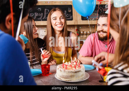 Cheveux longs Brunette girl sitting autour de ses amis et de sourire un lot sur un anniversaire Banque D'Images
