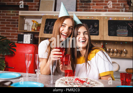 Brunette copines dans les chapeaux de fête holding drinks et celebrating birthday Banque D'Images