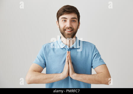 Bouddhistes jeunes prêts à inhaler la connaissance. Portrait of cute happy guy holding européen réuni plus de poitrine, comme le palm si priant dans un style asiatique debout sur fond gris, exprimer la confiance et la joie Banque D'Images