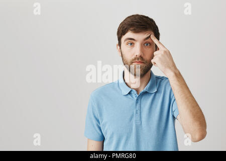 Bon calme-à la levée de l'homme barbu sourcil avec index et debout avec poker face sur fond gris. Rude guy montre qu'il n'est pas surpris ou intéressé par conversation Banque D'Images